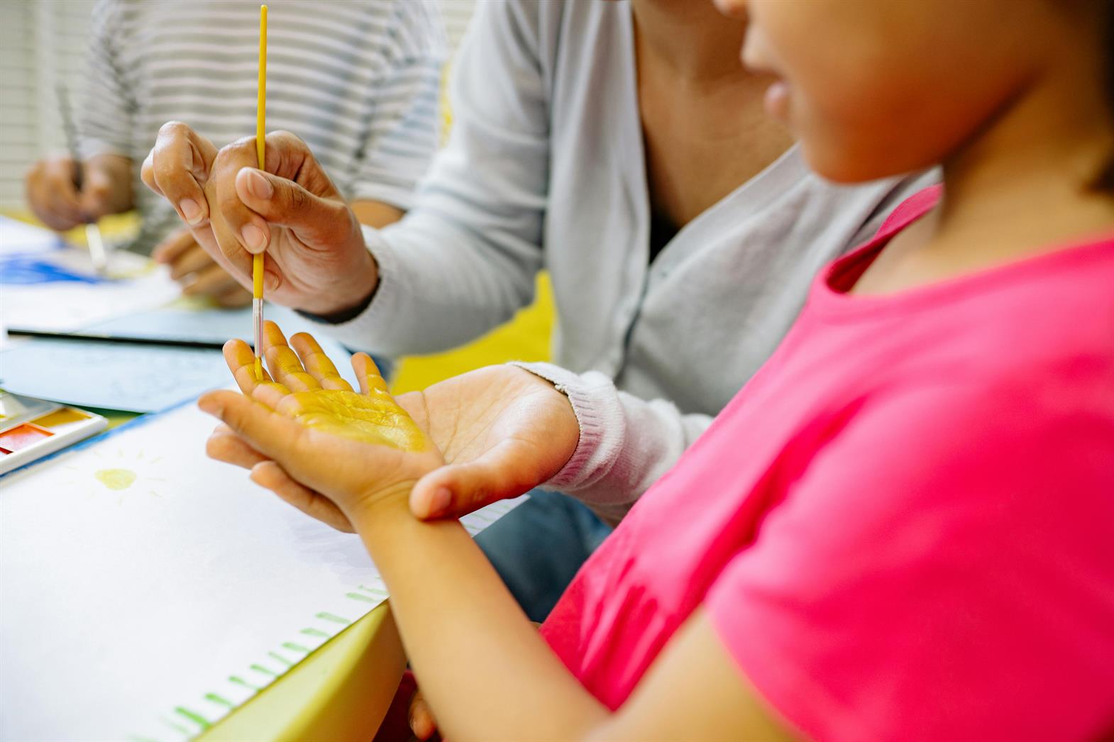 Person Painting A Girl's Hand With Yellow Color