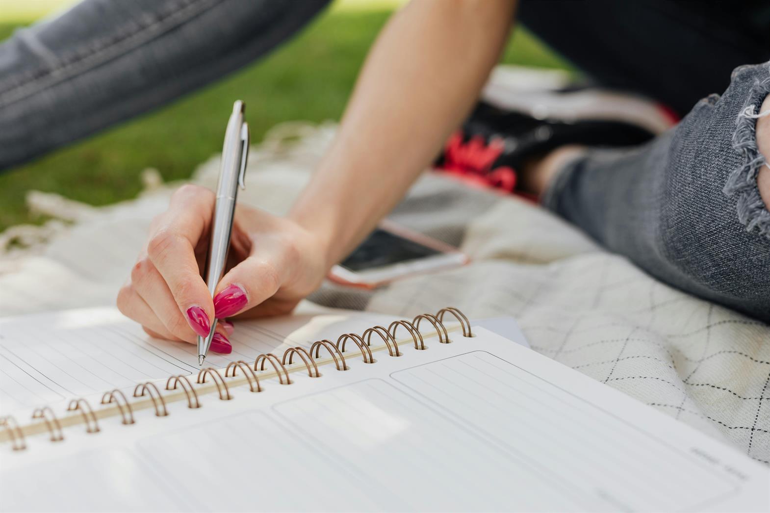 Gros plan sur la main d'une femme en train d'écrire dans un cahier dans un parc ensoleillé
