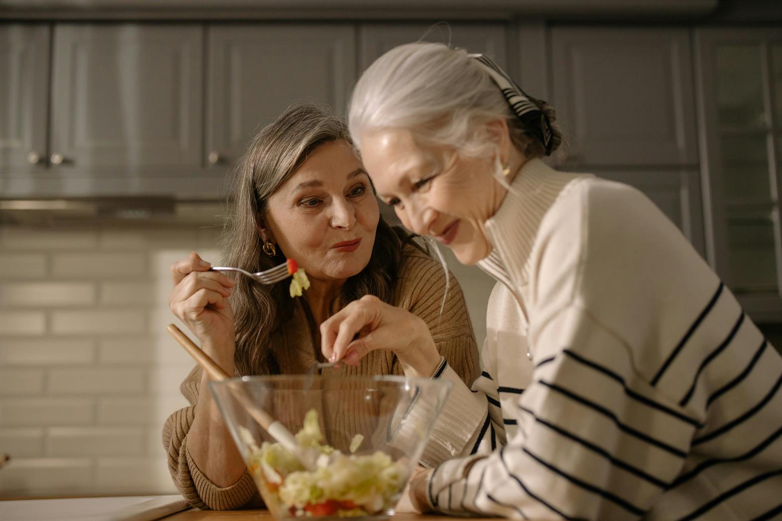 Two senior women eating salad in a kitchen