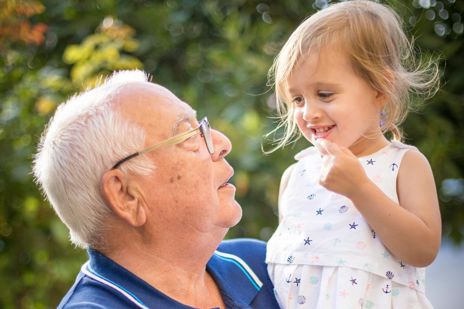 A grandfather holding his granddaughter in a garden