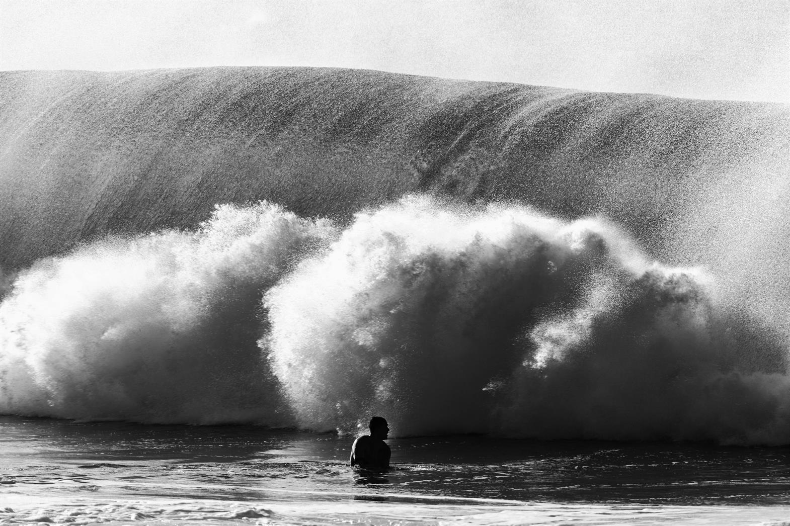 Silhouette d'une personne dans l'océan, debout devant une grande vague.