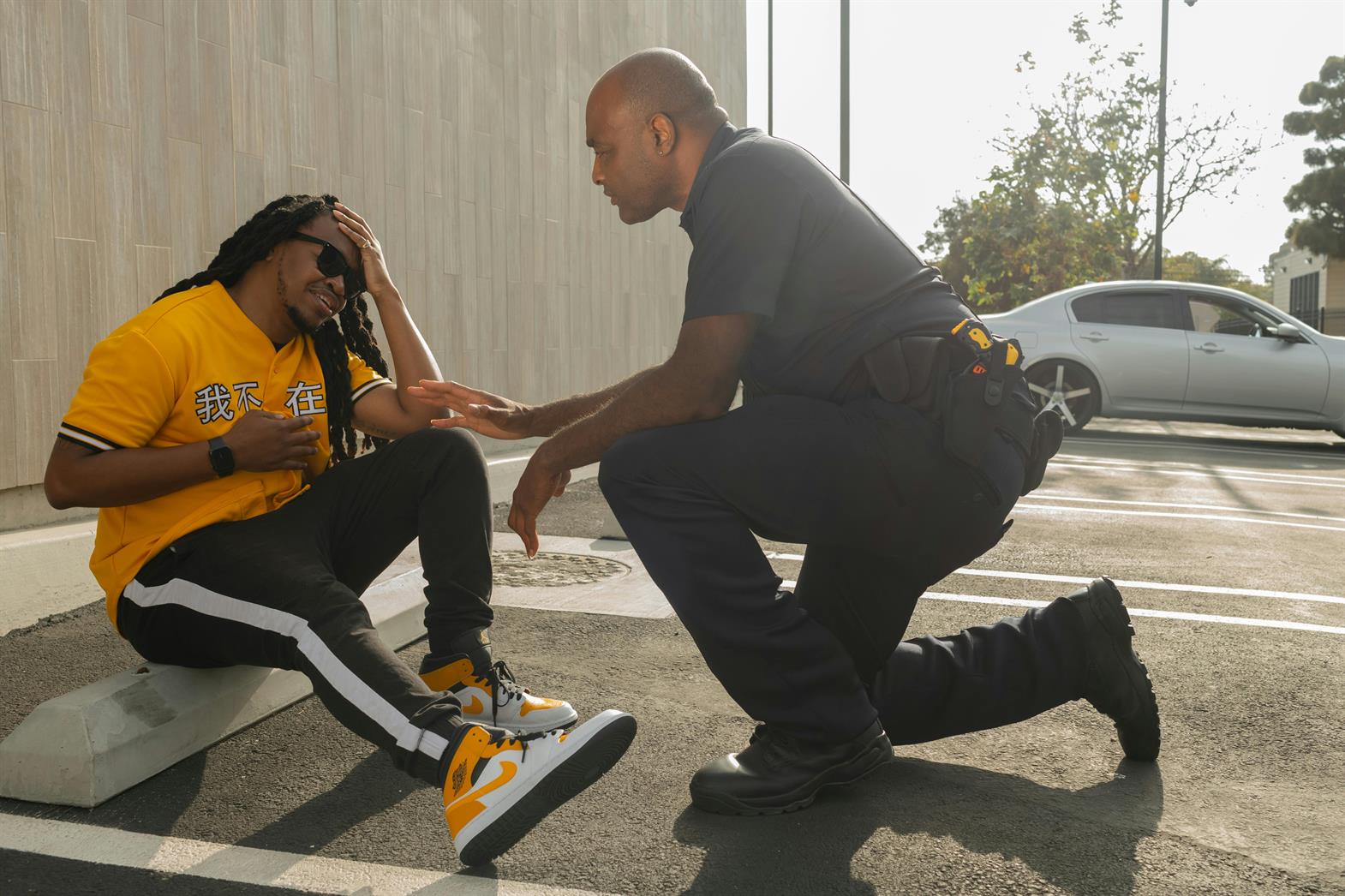 A police officer kneeling down to help a man sitting on a curb
