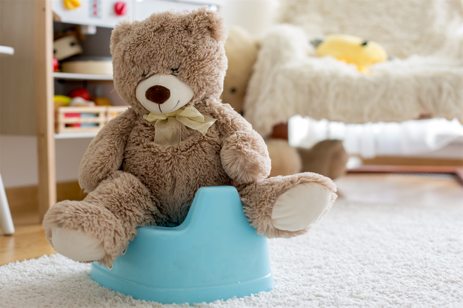 Un ours en peluche brun assis sur des toilettes bleues pour enfants.