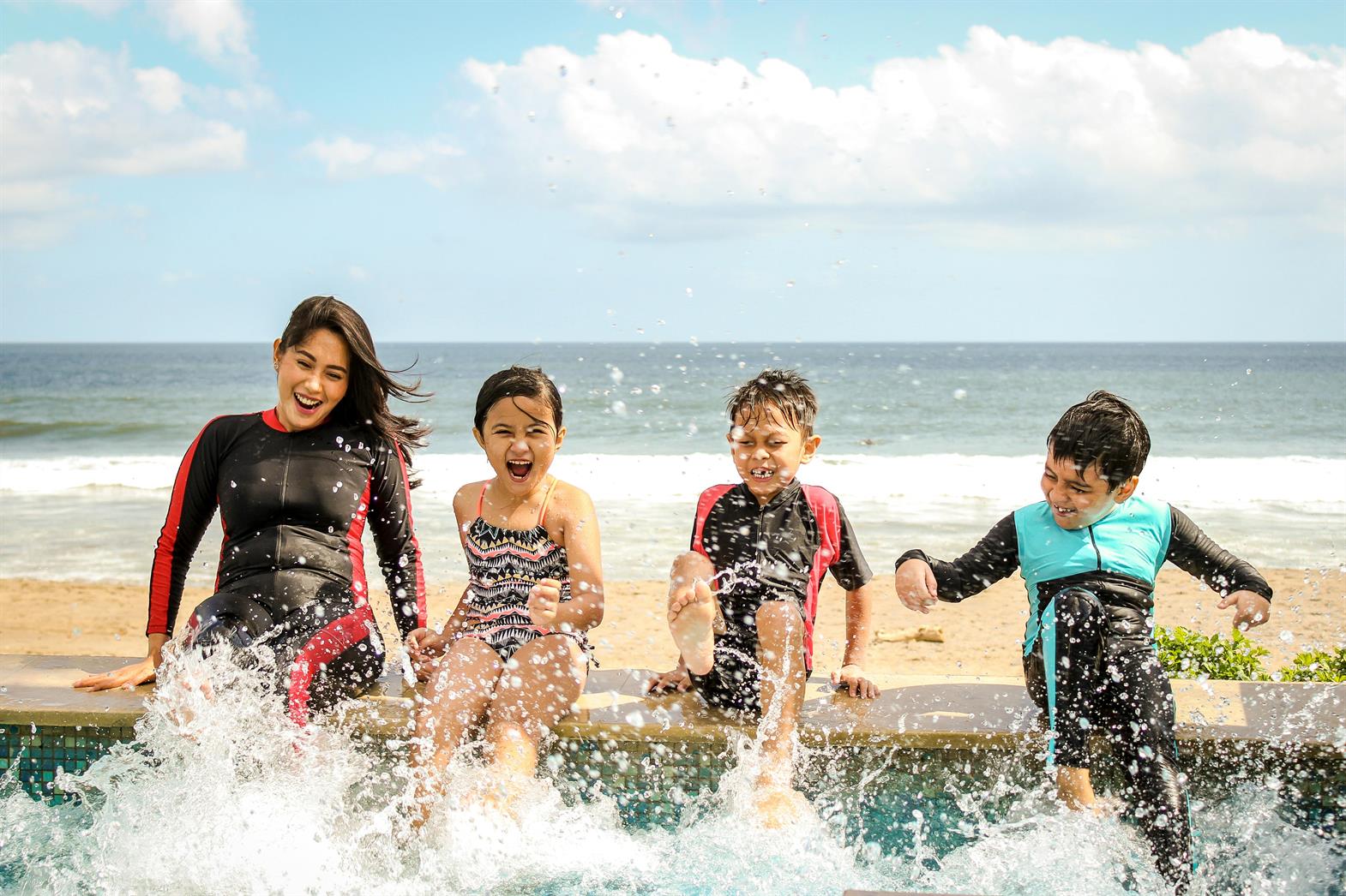 A family splashing and laughing in a pool near a beach