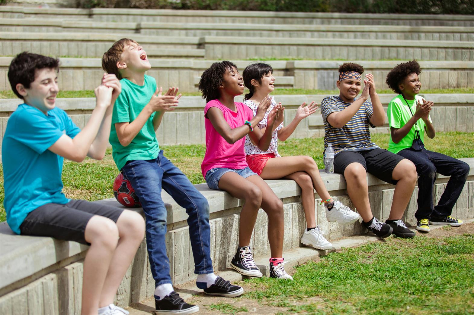 A group of children joyfully clapping and cheering together while sitting outdoors