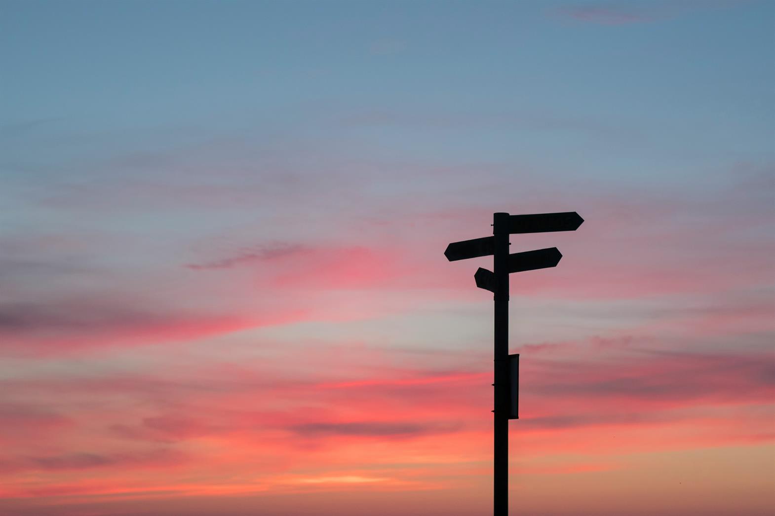 A silhouette of road sign post at sunset