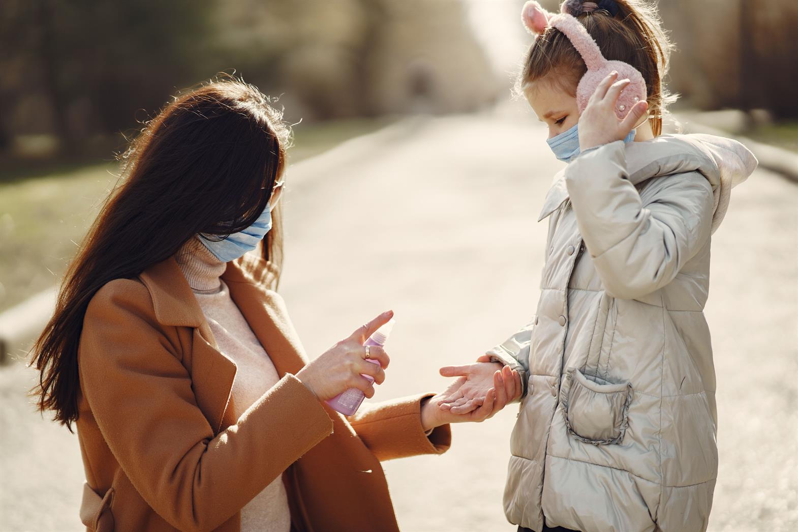  A mother helps her daughter sanitize hands while wearing masks in a sunny park