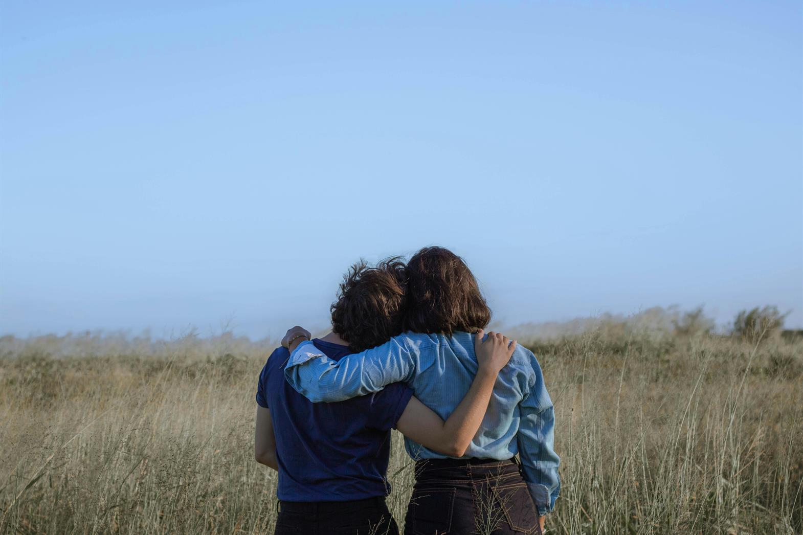 Two people leaning against each other in a meadow