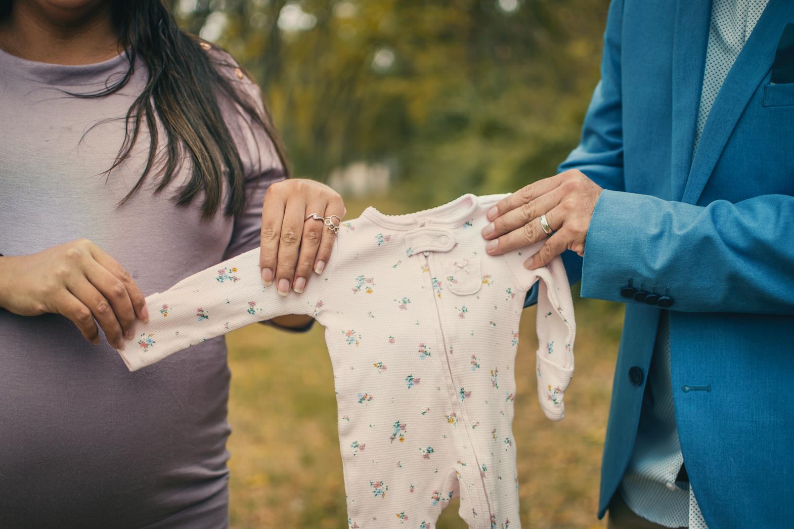 A man and a woman hold up a baby's onesie