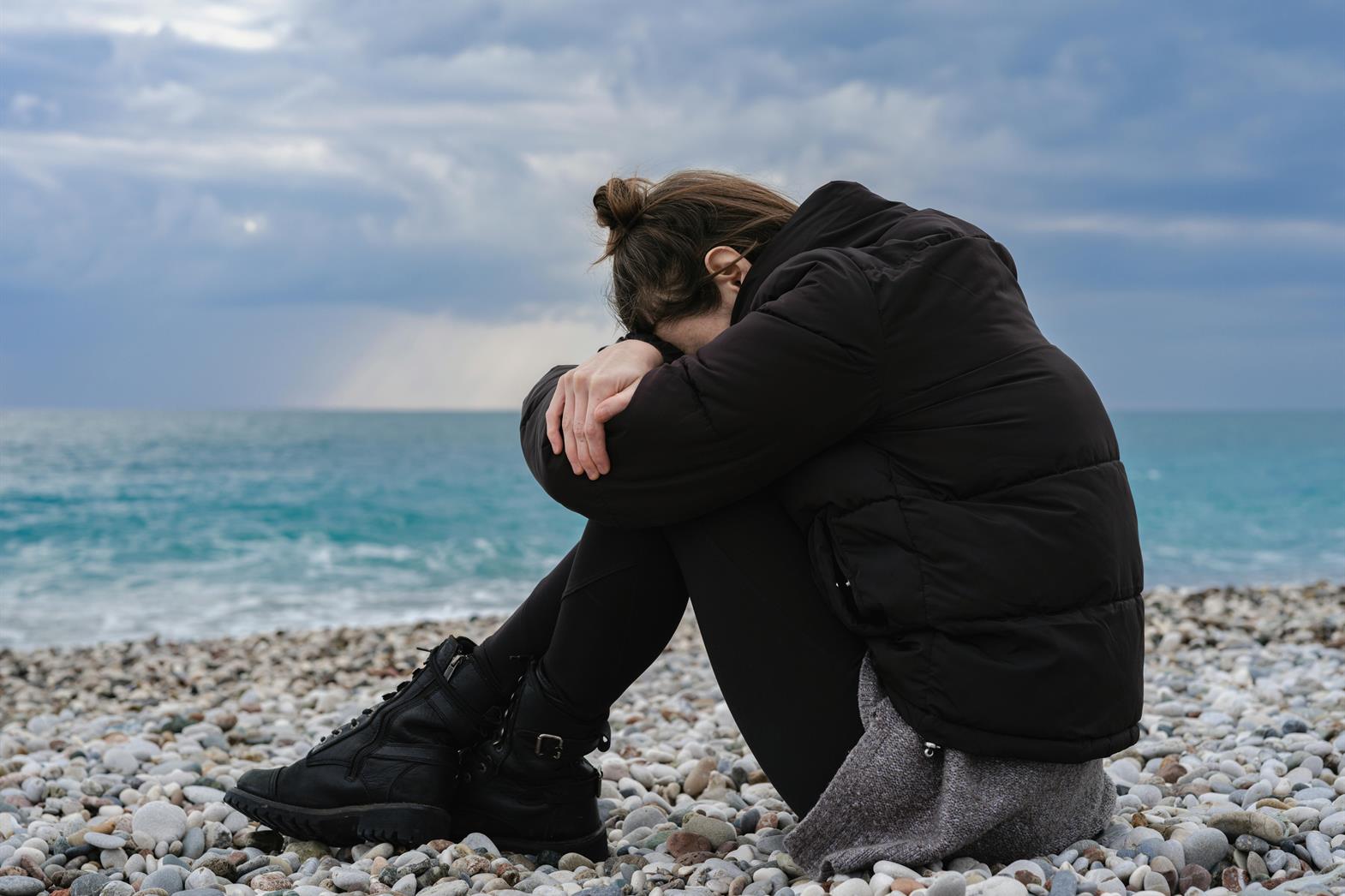 Woman Wearing Jacket Sitting on Rocky Shore