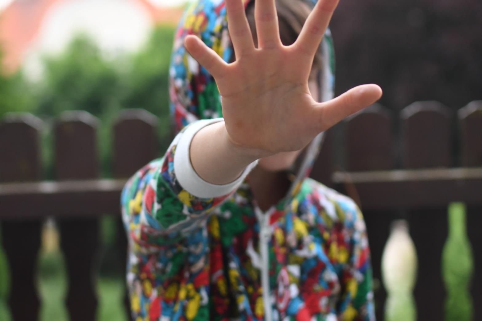 A person wearing a colorful hoodie holding hand out in a stopping gesture