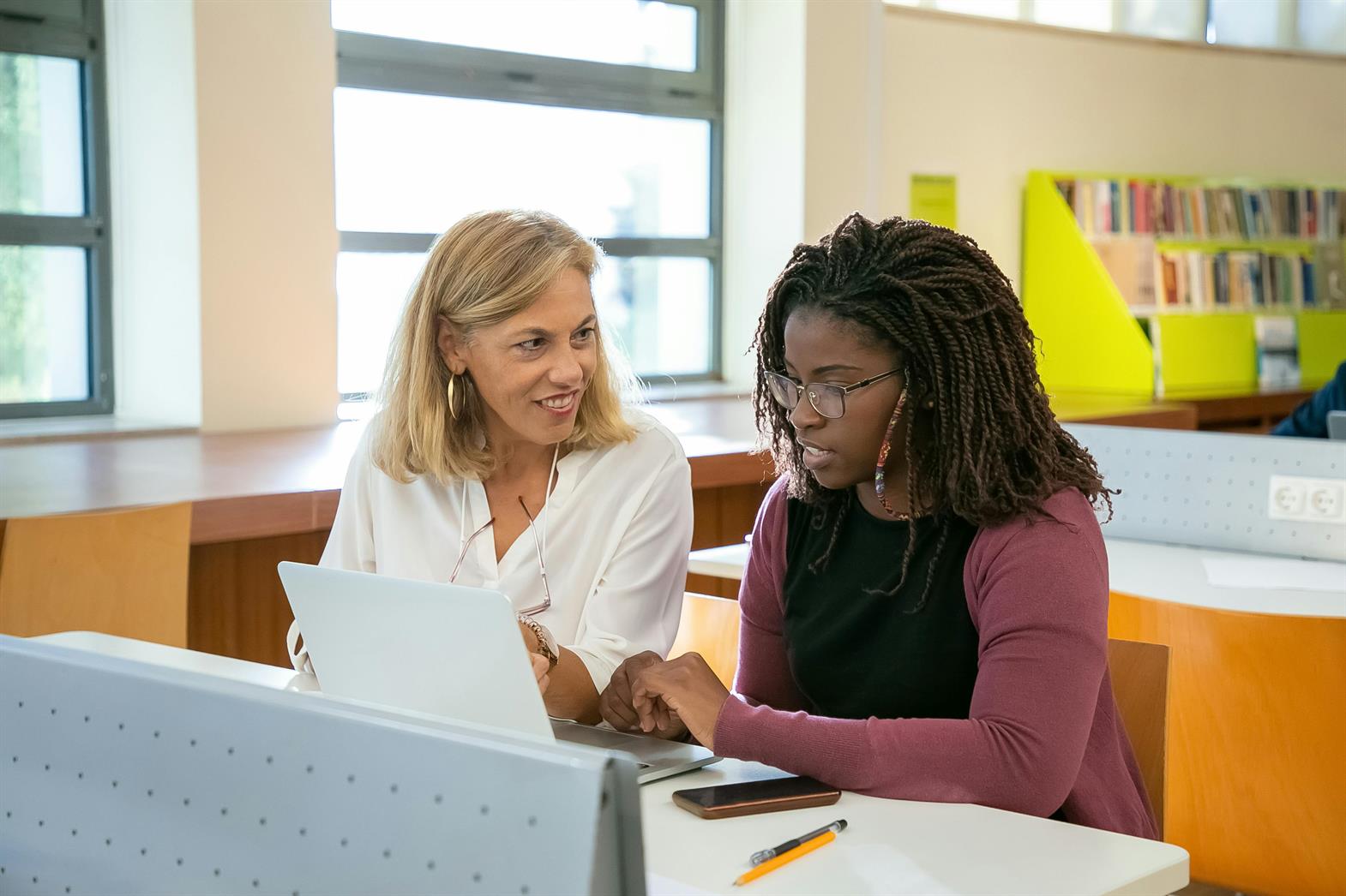 An advisor talking with a student using a laptop in a university library