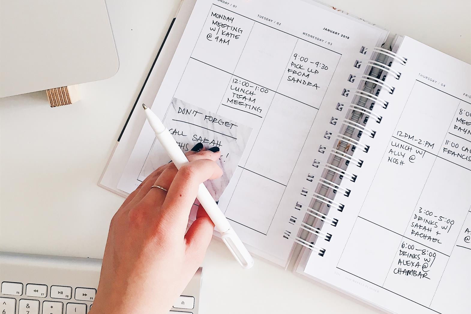 A person holding a pen while reviewing their planner
