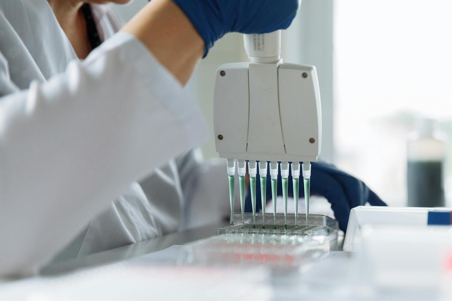 A scientist wearing a lab coat uses a pipette in a lab