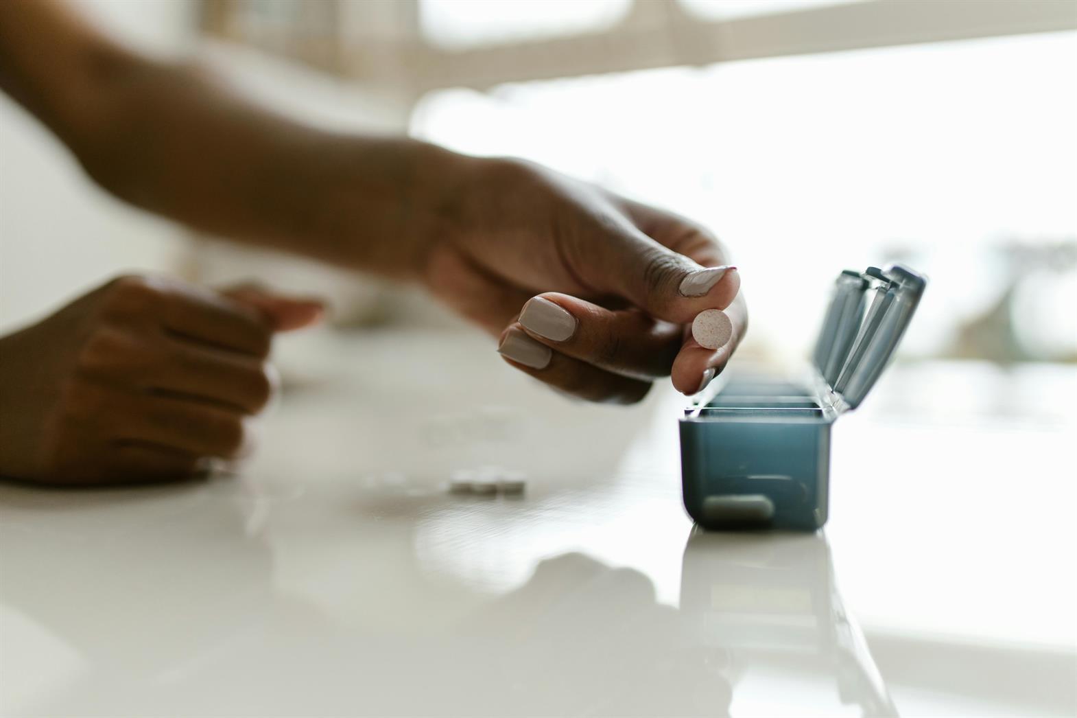 A hand placing pills in a weekly organizer
