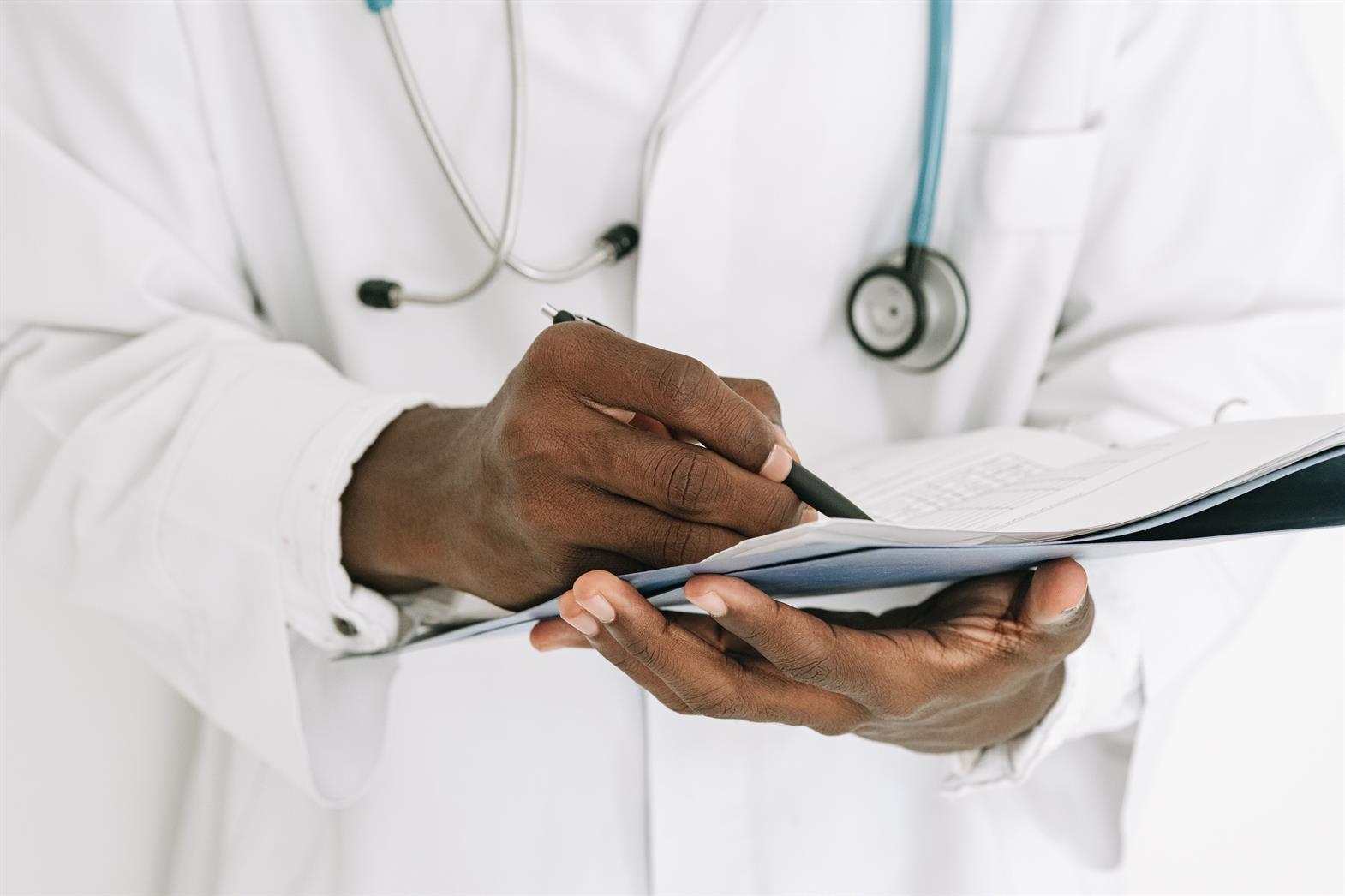 A doctor wearing a white lab coat writing on a clipboard