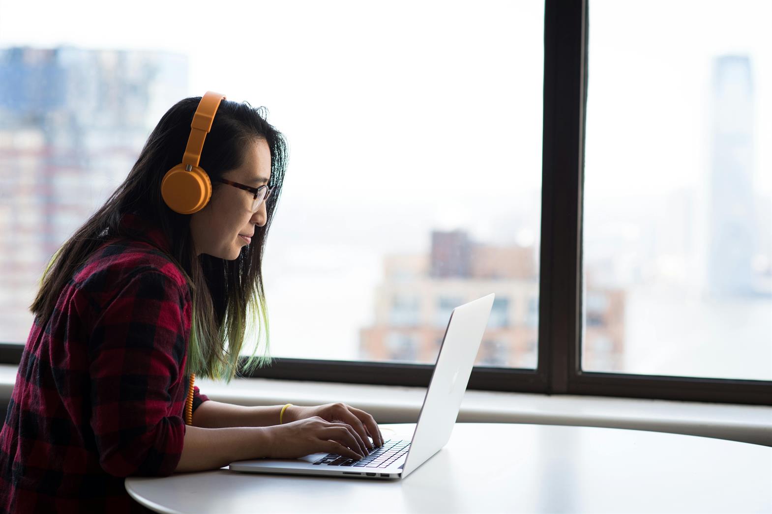 A person with headphones using laptop for remote work in a city setting